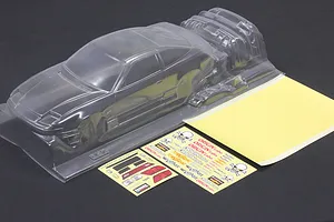 Unpainted clear RC car body shell with separate parts, decal sheets, and masking sheet on a dark background.