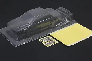 Unpainted clear polycarbonate RC drift car body shell with a mask sheet and decal sheet on a dark surface.