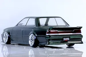Rear three-quarter view of a dark metallic green RC drift car body shell mounted on a chassis with custom wheels against a white background.