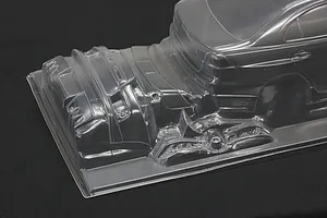 Unpainted clear polycarbonate RC car body shell showing rear section and molded bumper parts on a dark background.