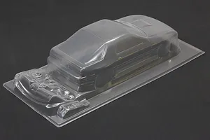 Unpainted clear RC car body shell for a Mazda RX-7 on a dark background, showing molded details and additional parts.