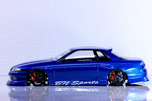 Side profile of a blue Pandora RC HCR32 2Dr drift car body shell with BN Sports graphics, black wheels, and red brake calipers on a reflective surface.