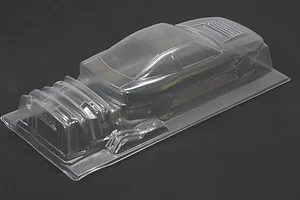 Clear unpainted polycarbonate RC car body shell on a dark surface, showing molded coupe and accessories.