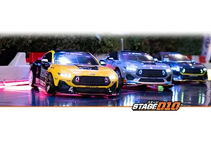 Three RC drift cars, including a yellow and black Mustang GT, driving on a reflective track with illuminated headlights.