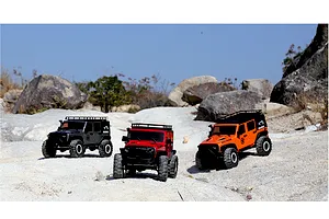 Three RGT Rock Cruiser Evolution V3 1/10 scale RC crawlers in black, red, and orange parked on a rocky outdoor terrain.