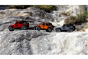 Three RGT Rock Cruiser Evolution V3 RC rock crawler models in red, orange, and grey parked on rocky outdoor terrain.