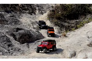 Three 1/10 scale RGT Rock Cruiser Evolution V3 RC rock crawlers in red, orange, and black navigating a rocky outdoor trail.