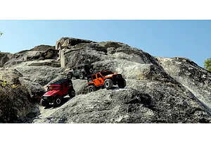 Three RGT Rock Cruiser RC rock crawler models in red, orange, and grey navigating a rocky outdoor terrain.
