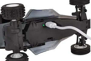 Bottom view of the Team Associated RC28 RC buggy showing a USB charging cable plugged into the chassis with a green indicator light.