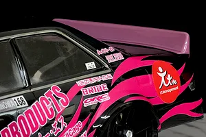 Close-up rear quarter view of a black and pink RC drift car featuring a large pink ducktail spoiler mounted on the trunk.