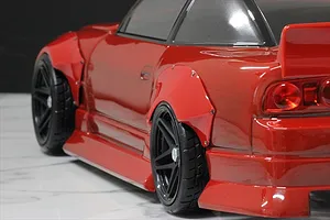 Close-up of a red RC drift car body installed with wide over fender flares over black wheels and rubber tires.