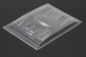 Unpainted clear polycarbonate RC body shell accessory sheet with various molded duct and vent parts on a dark surface.