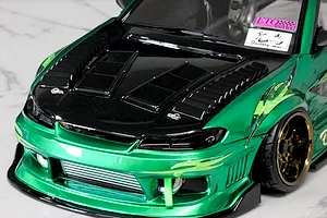 Close-up of a green RC drift car body shell featuring black hood vents and aftermarket duct parts installed on the front end.