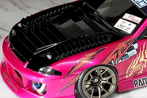 Close-up of an RC car body shell featuring black hood vents, a pink and black painted finish, and custom decals.