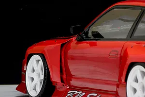 Close-up side view of a red RC drift car body showing installed over fender flares and white wheels against a dark background.