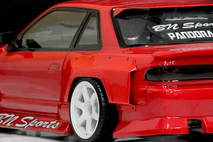 Close-up view of a red RC drift car body installed with wide over-fenders and white wheels against a plain background.