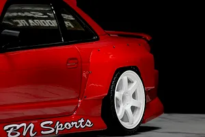 Close-up of a red RC car body showing the rear fender flare installed over the rear wheel, featuring visible mounting screw details.