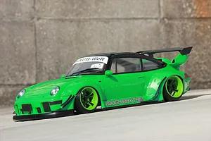 Bright green RC drift car body featuring wide fenders and a black rear wing on an outdoor concrete surface.