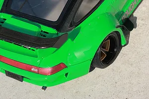 Close-up of the rear quarter section of a bright green RC car body featuring wide fender flares, a black spoiler, and deep dish wheel.