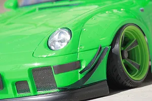 Close-up of a bright green RC car body featuring a wide fender set, front canards, headlight, and custom wheel.