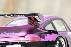 Close-up of a purple RC car body shell showing the rear wing, wide fender, and RWB lettering on the decklid.