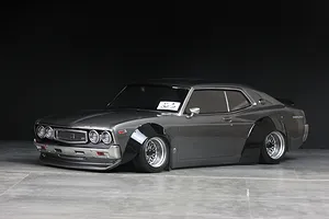 Grey RC drift car body shell featuring prominent black overfenders and mesh wheels against a dark background.