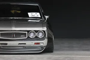 Close-up front view of an RC car body shell featuring overfenders, dual headlights, a front grille, and a bumper against a dark background.