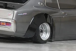 Close-up view of a dark grey RC car body shell fitted with a black overfender flare over the rear wheel and mesh rim.