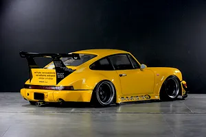 Rear-three-quarter studio shot of a yellow Pandora RC RWB 993 type RC body shell with a large rear wing and black wheels.