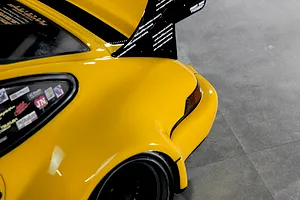 Close-up of the rear quarter, fender, and large wing of a yellow Pandora RC RWB 993 body shell on a grey floor.