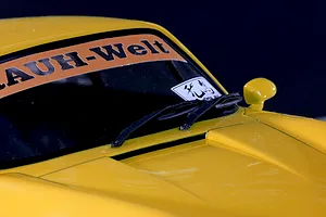 Close-up of a yellow RC car body shell showing the windshield, wipers, side mirror, and Rauh-Welt windshield banner.