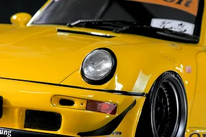 Close-up of the front left section of a yellow RWB 993 RC car body shell showing the headlight, bumper, and wheel.