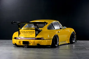 Rear three-quarter view of a yellow Pandora RC RWB 993 Type model car with wide fenders and a large wing on a dark background.