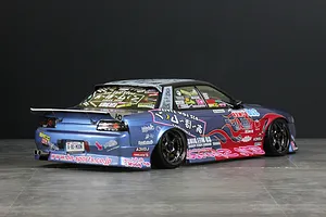 Rear-three-quarter view of a customized blue RC drift car body with extensive sponsor decals and a large rear wing.