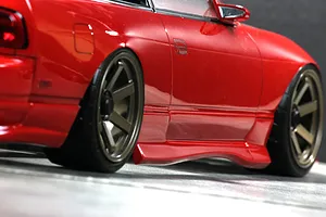 Close-up side profile view of a red RC drift car body showing custom wheels, side skirt, and low stance.