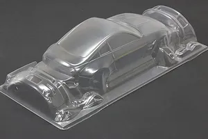 Unpainted clear polycarbonate RC car body shell on a dark surface, showing front and rear bumper parts molded into the sheet.