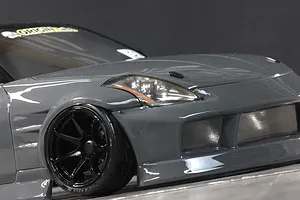 Close-up of the front left quarter of a grey RC drift car body showing the front wheel and headlight assembly.