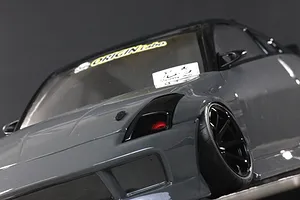 Low angle close-up of the front quarter of a glossy grey RC drift car body with black wheels and tinted windows.