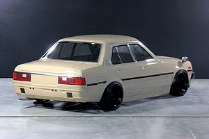 Rear three-quarter studio view of a painted tan Toyota Corolla KE70 RC drift car body on a grey surface.