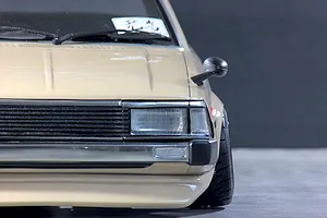 Close-up front quarter view of the beige Toyota Corolla KE70 RC body shell, highlighting the grille, headlight, and fender mirror.
