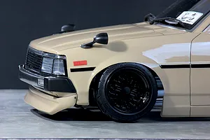 Close-up of the front quarter of a beige RC drift car body with black wheels and fender mirrors.