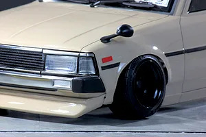 Close-up front quarter view of a beige Toyota Corolla KE70 RC drift car body with black wheels and fender mirror.