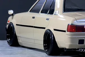 Close-up side profile of a beige Toyota Corolla KE70 RC drift car body with black wheels and deep dish rims.