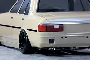 Close-up rear quarter view of a cream-colored Toyota Corolla KE70 RC drift car body showing dual exhaust pipes, deep dish wheels, and tail lights.