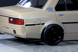 Close-up rear quarter view of a tan RC drift car body shell showing the tail light, rear wheel, and black mesh rim.