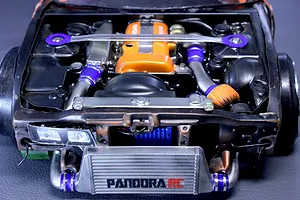 Top-down view of a detailed scale model RC car engine bay with an orange valve cover, front mount intercooler, and strut bar installed.