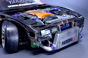 Close up view of a detailed scale RC model car engine bay featuring an orange valve cover, front intercooler with Pandora RC branding, and suspension components.
