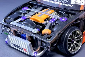 Close-up of a detailed model car engine bay featuring an orange valve cover, front intercooler with Pandora RC branding, and a strut bar.