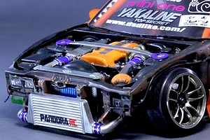 Close-up view of a detailed RC drift car engine bay with an orange valve cover, intercooler, and strut bar installed.
