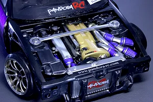 Close-up of a detailed Pandora RC scale model car engine bay installed in a vehicle, featuring a gold valve cover and strut bar.